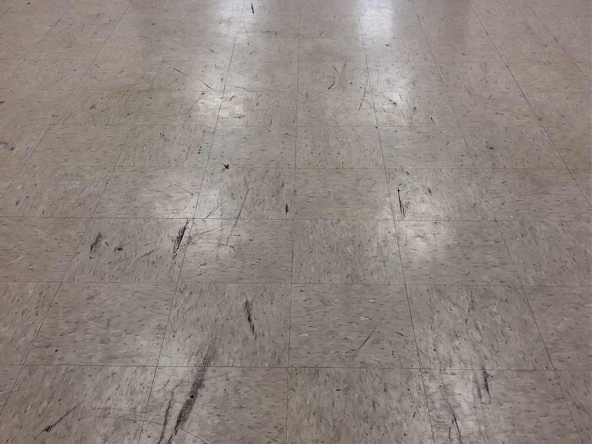 A vinyl tile corridor before stripping: scratches, heel marks and a dull finish